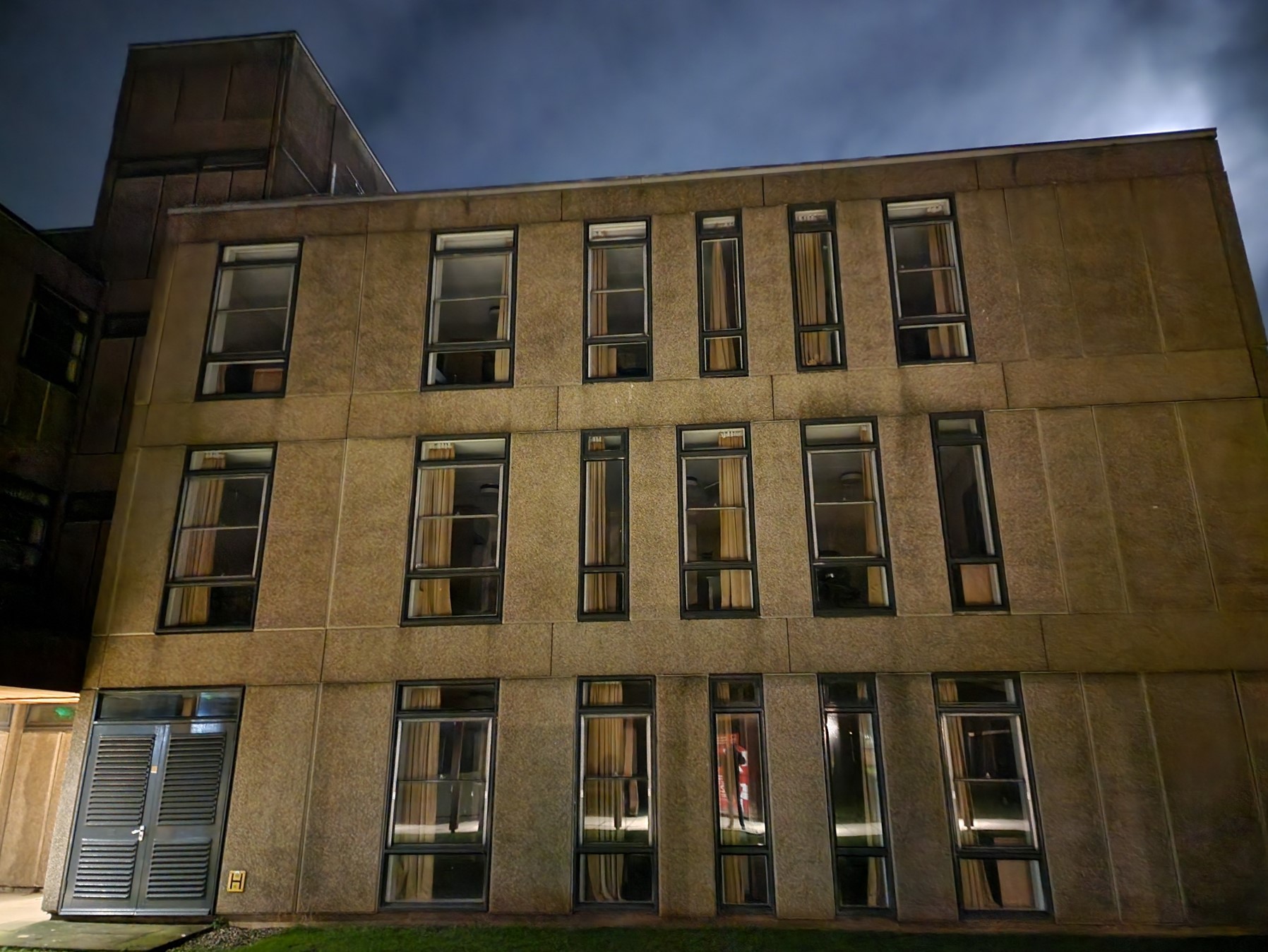 An abandoned 3 storey concrete building at night with many darkened windows