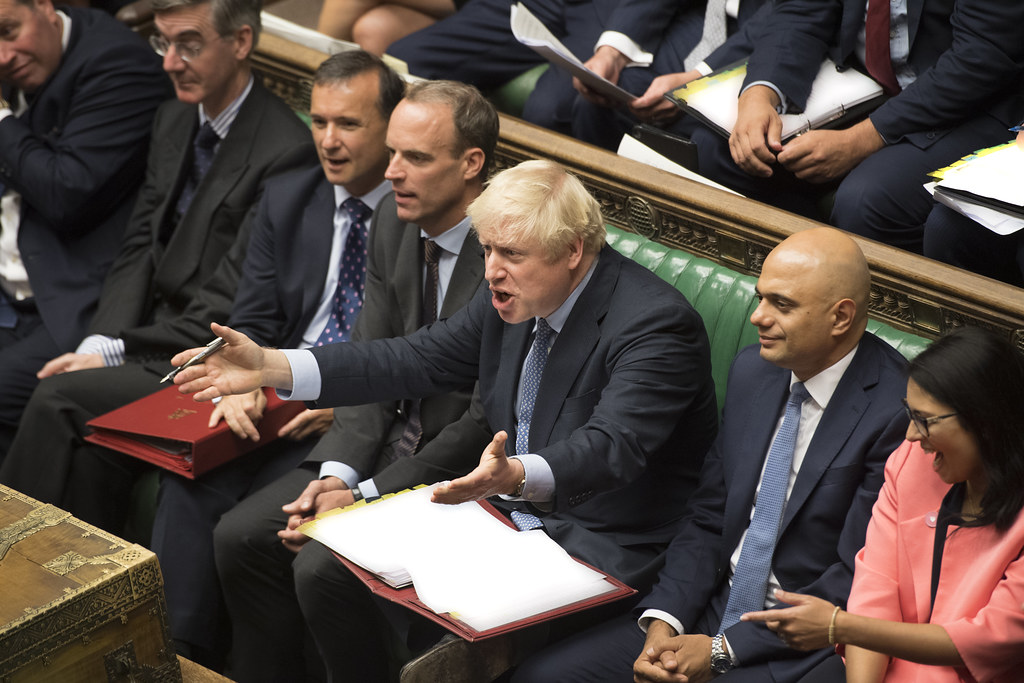 Boris Johnson sitting in the House Of Commons with his mouth open and his arms outstretched infront of him